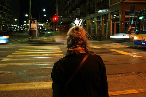 Elderly woman crossing city intersection.